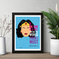Framed poster of Wonder Woman with a quote on a blue background, placed on a wooden surface with plants.